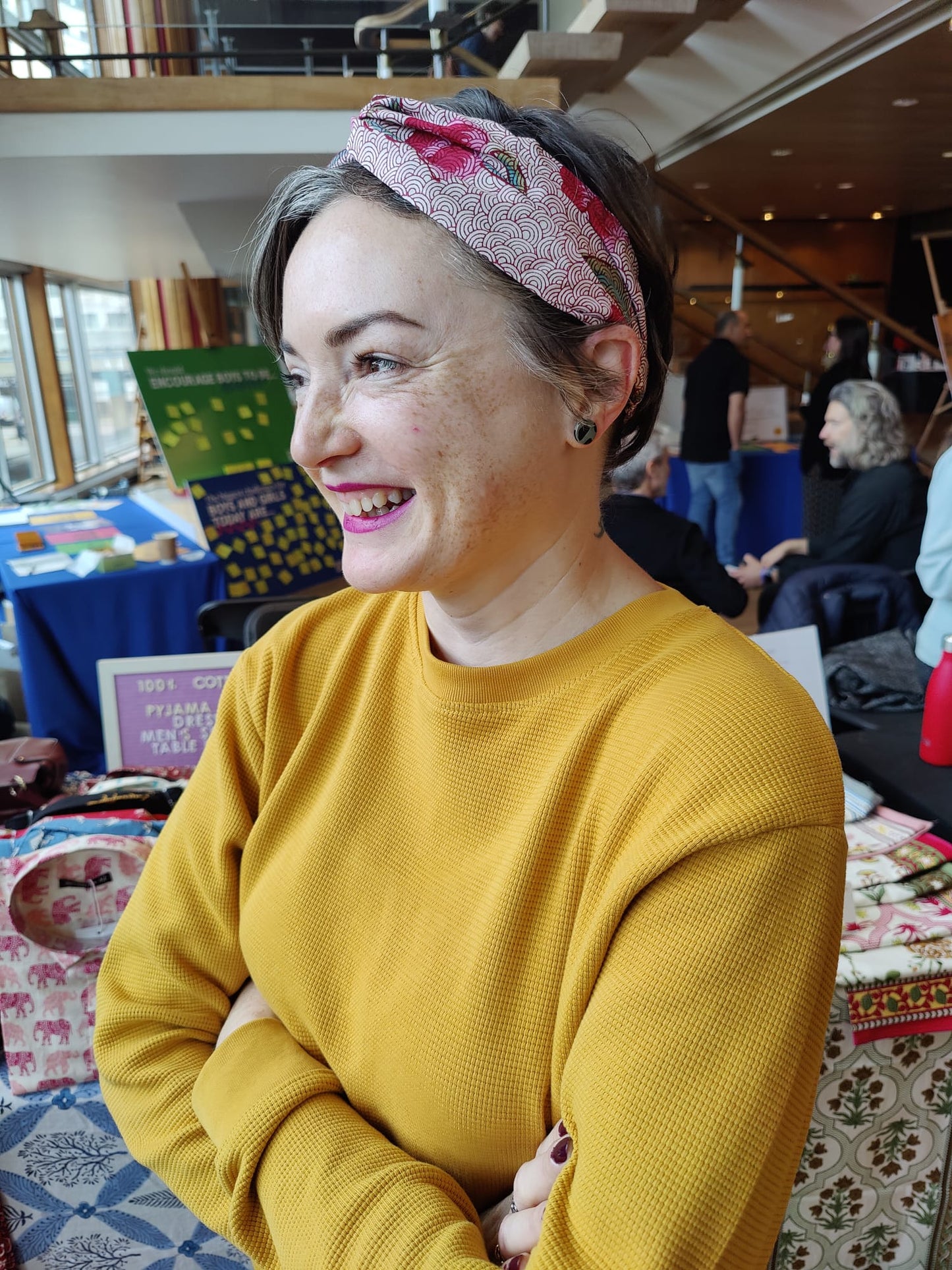 Lady wearing a yellow jumper and red headband, smiling and looking away from the camera.away from 
