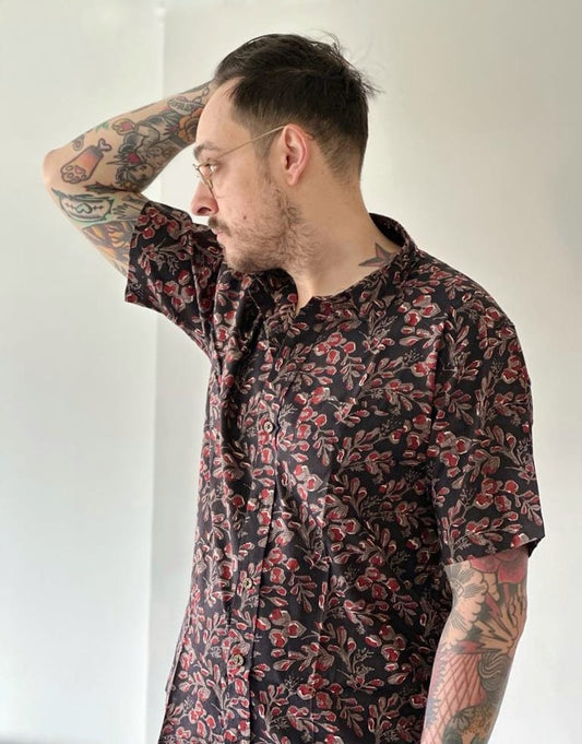 Male model with glasses and tatoo posing in a black and red floral shirt.