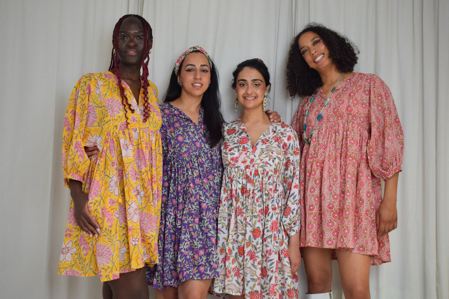 four girls wearing floral cotton mini dress infront of a white curtain.
