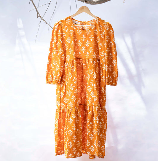 orange tiered midi dress hanging on a wooden hanger infront of a white background