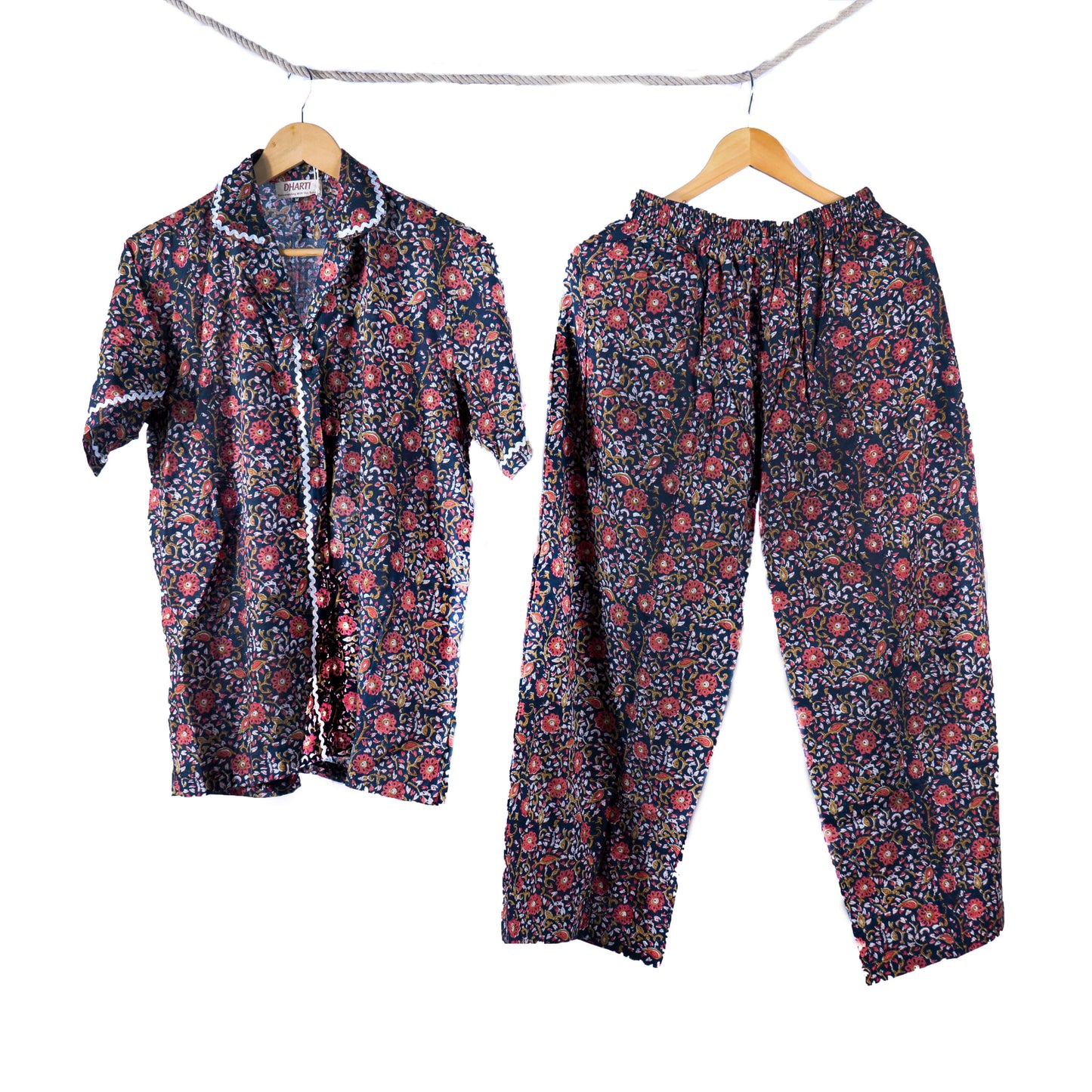 A navy handblock printed floral shirt and pyjamas hanging on hangers by a rope.