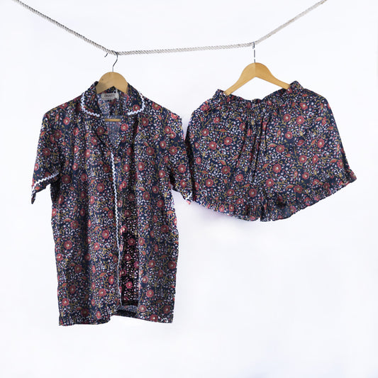 A navy handblock printed floral shirt and matching shorts hanging on hangers by a rope.